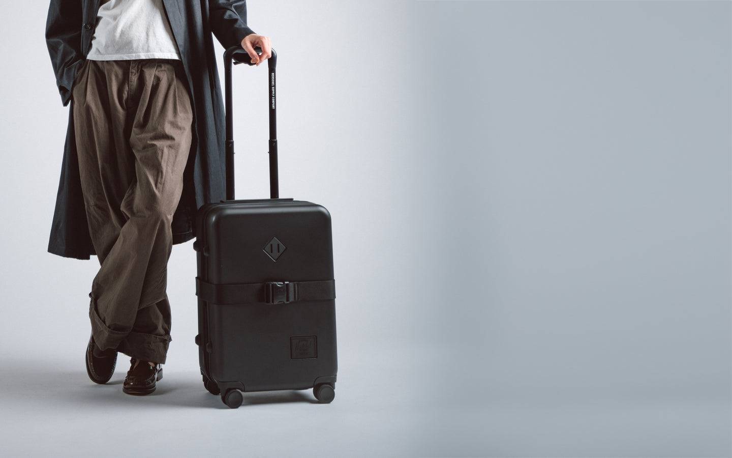 Herschel Heritage Hardshell Large Carry On Expandable luggage in black, showcasing a durable textured exterior and sleek telescoping handle.